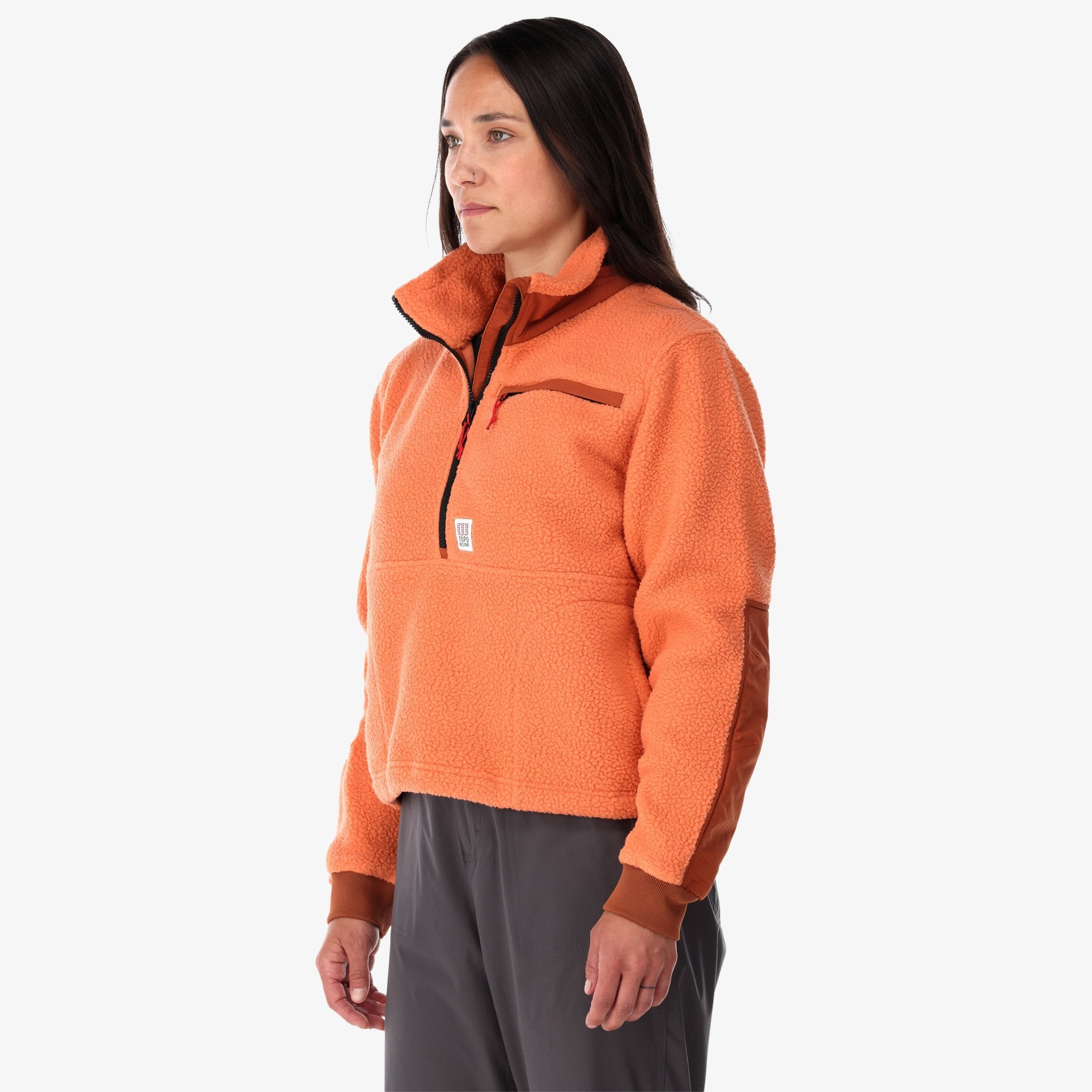 Side shot of Topo Designs Women's Mountain Fleece Pullover in "Rust / brick" pink orange on model.