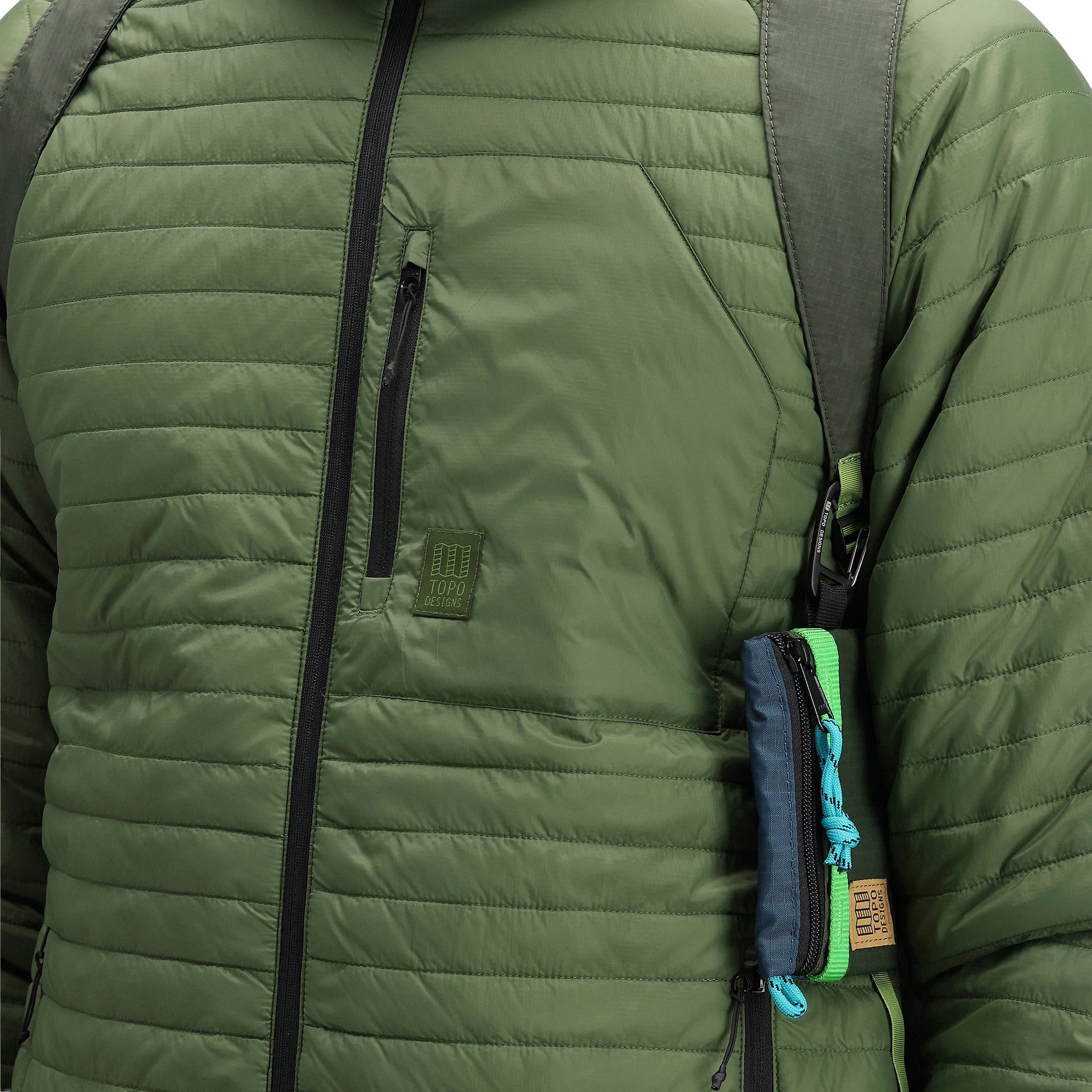 General detail shot of chest pocket and logo patch on model wearing Topo Designs Men's Global Puffer packable recycled insulated Hoodie jacket in "olive" green.