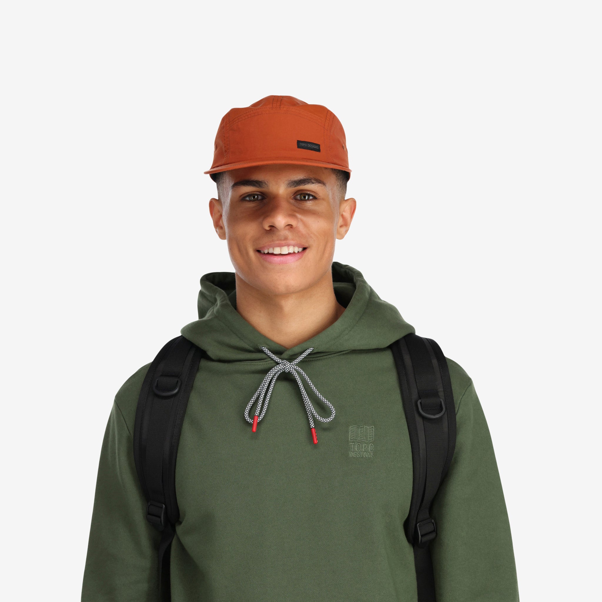 General front model shot of Topo Designs Nylon Camp 5-panel flat brim Hat in "brick" orange