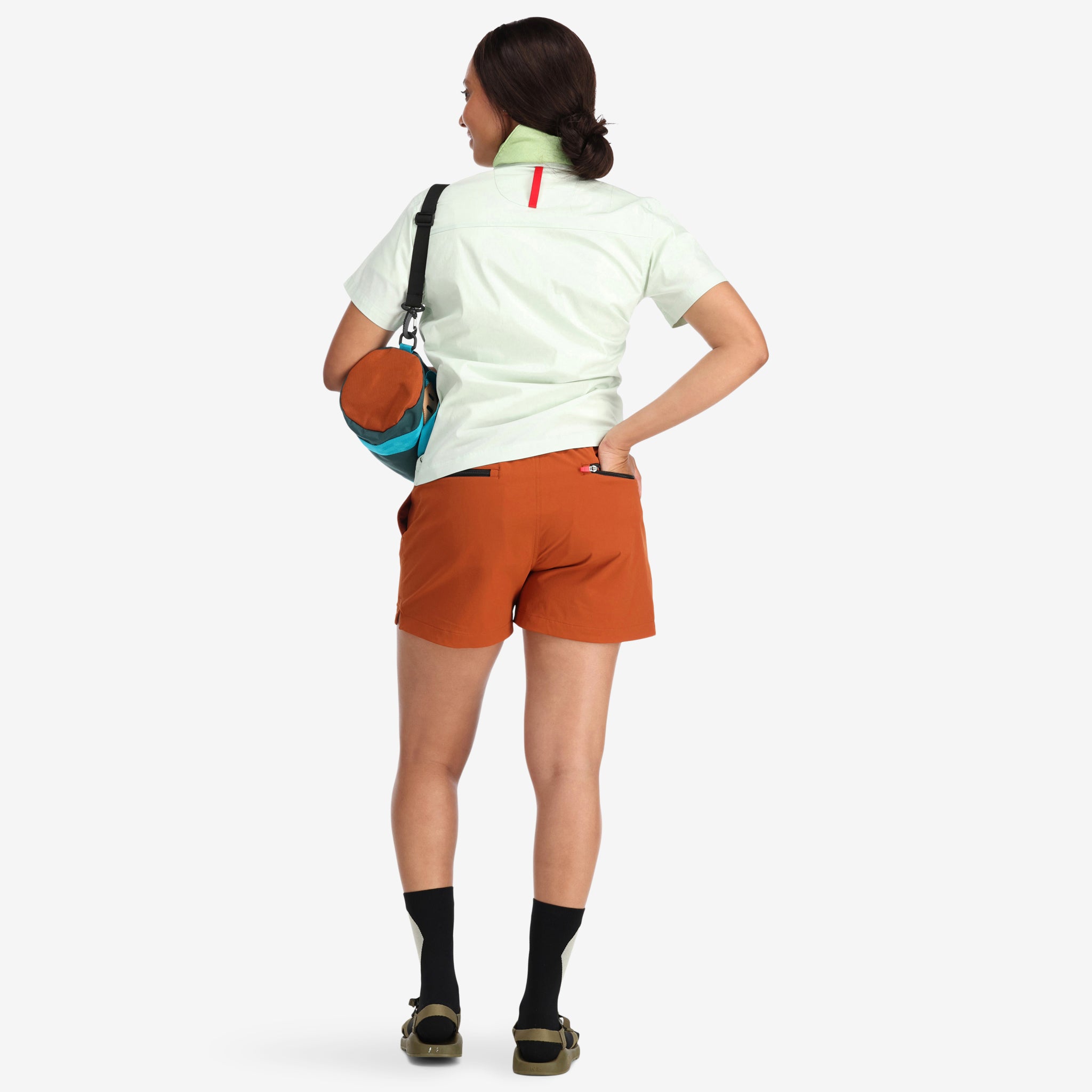 Back model shot of Topo Designs Women's Global lightweight quick dry travel Shorts in "Brick" orange. Show on "slate" "pond blue" & "olive"