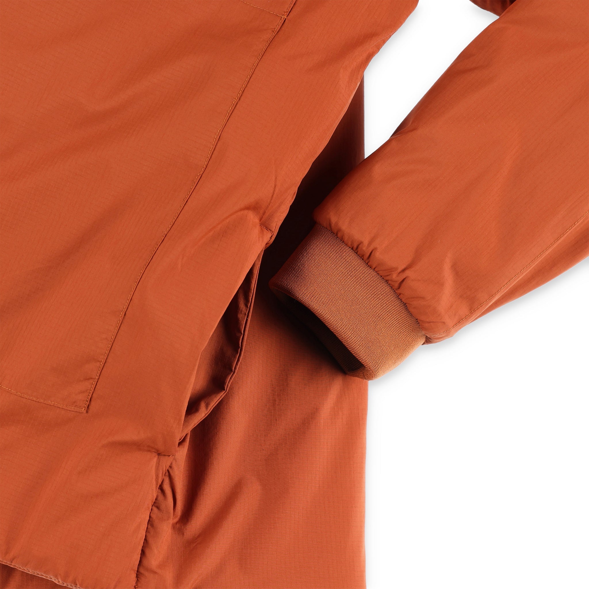 General detail shot of hand pockets and cuff on Topo Designs Mountain Puffer Primaloft insulated Hoodie jacket in "Brick" orange