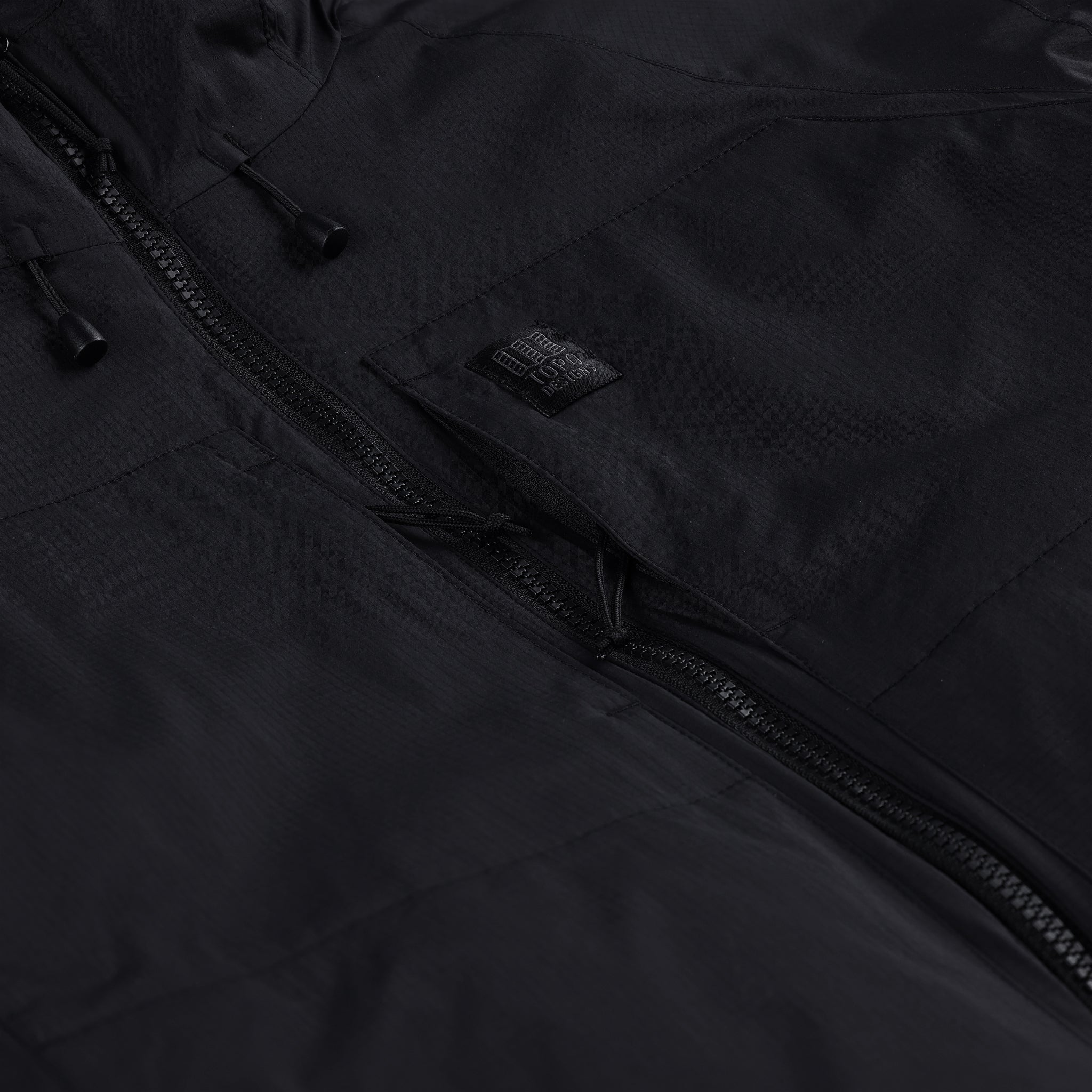 General detail shot of chest zipper pocket on Topo Designs Women's Puffer Primaloft insulated Hoodie jacket in "black"