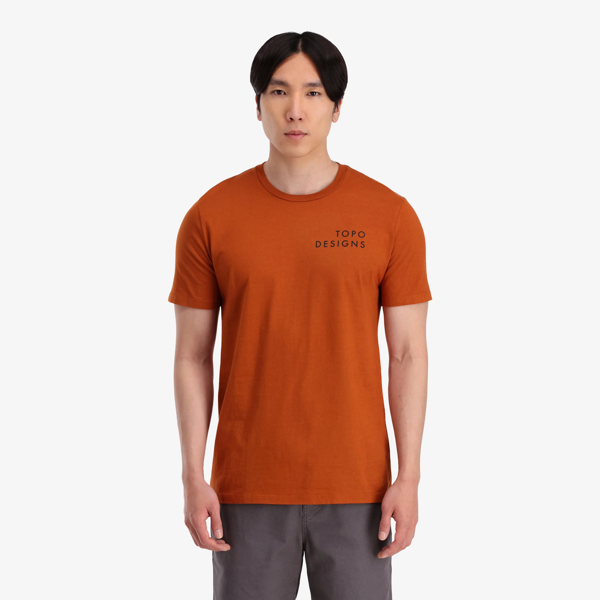 General shot on-model front view of Topo Designs Men's Camp Logo Tee 100% organic cotton graphic short sleeve t-shirt in "clay" orange.