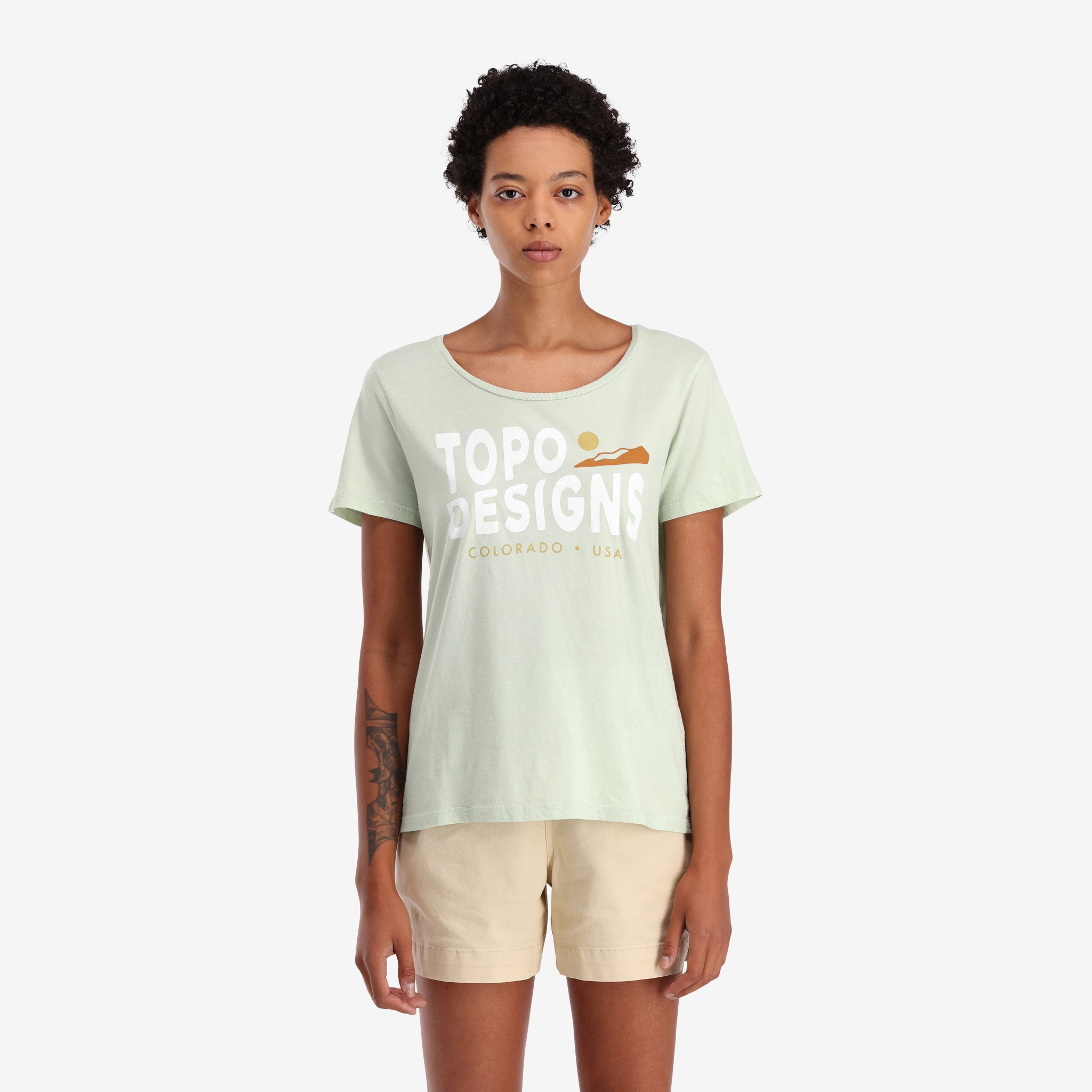 General shot On model front view of Topo Designs Women's Sunrise Tee 100% organic cotton short sleeve graphic logo t-shirt in "Light Mint" green..